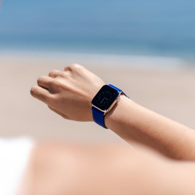Blueberry-Summer-Apple-watch-blue-fluo-band-on-a-feminne-tunned-wrist-with-the-sea-as-background